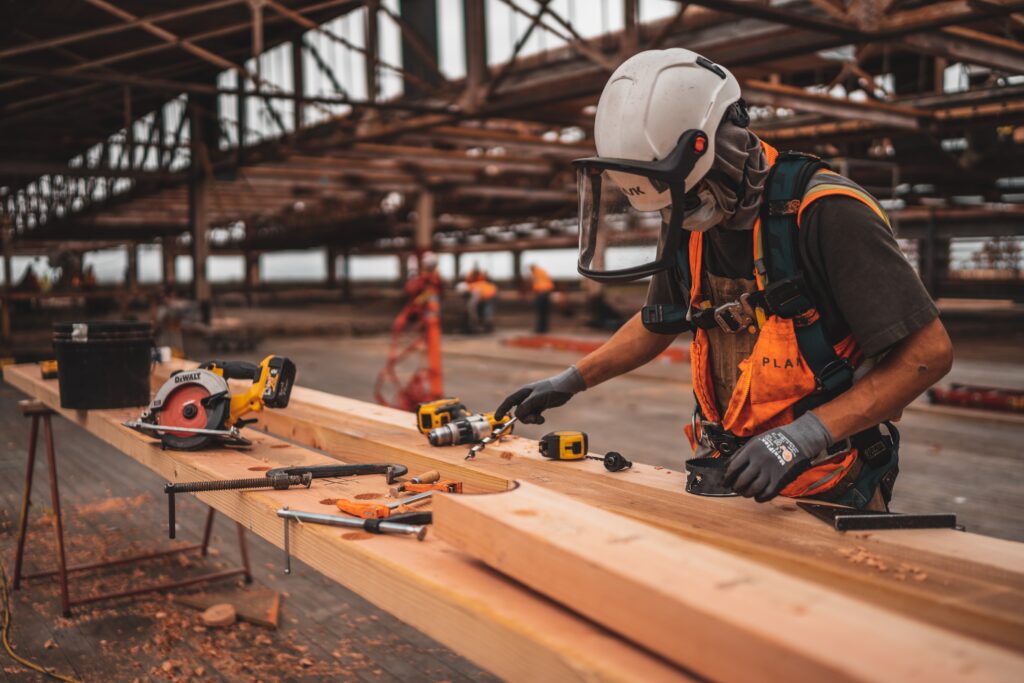 Trabalhador com equipamentos de segurança do trabalho (NRs 6) mexendo em pedaços de madeira. 